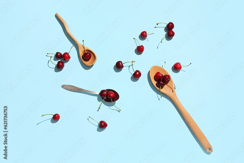 Spoons with sweet cherries on blue background