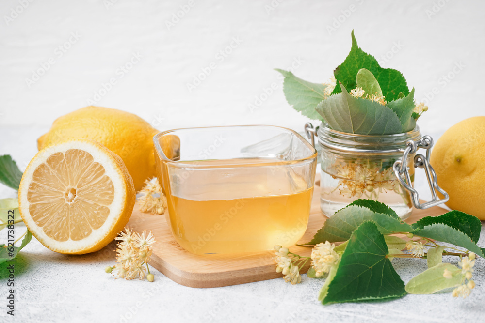 Wooden board with glass bowl of linden honey and lemon on white background