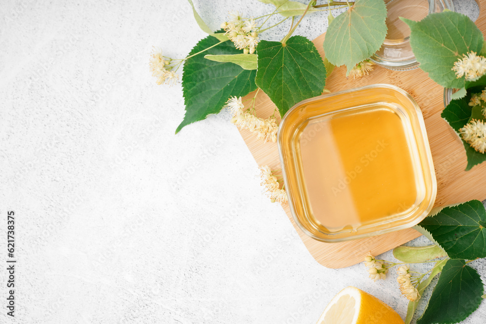 Wooden board with glass bowl of linden honey on white background