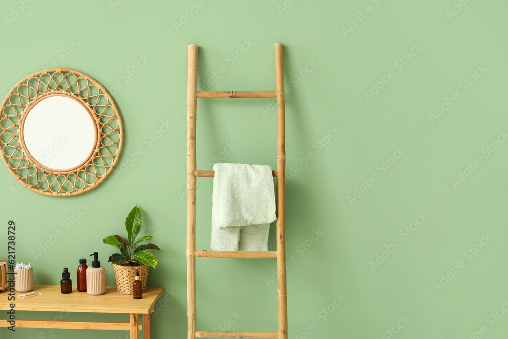 Wooden ladder, table with cosmetic products and mirror hanging on green wall in room