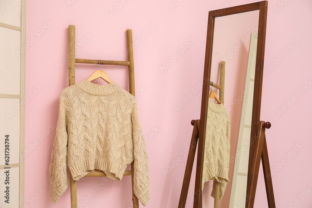 Sweater hanging on wooden ladder and mirror near pink wall in room