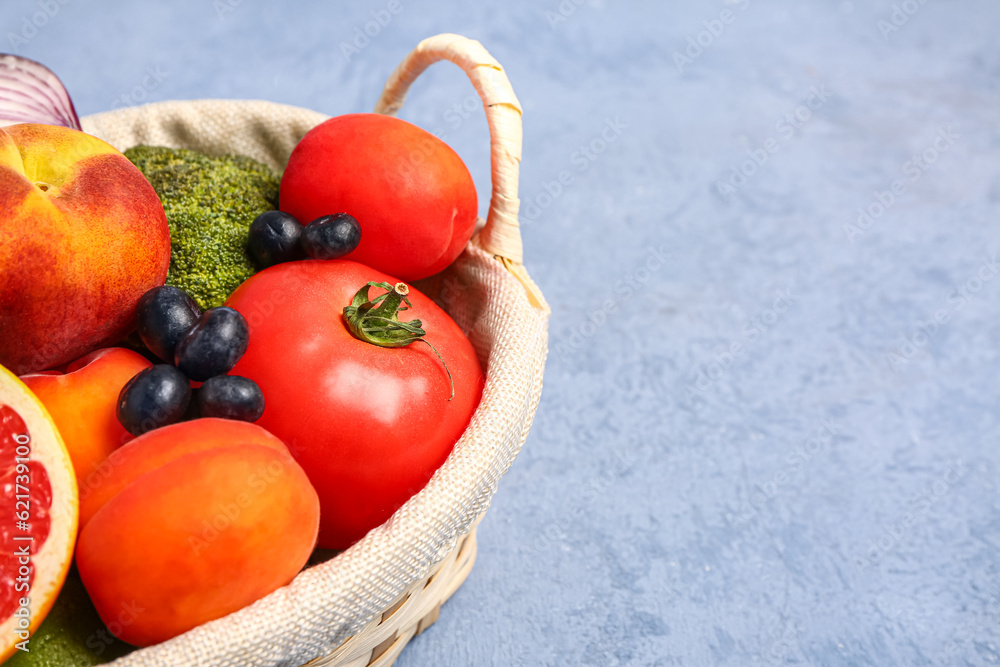 Wicker basket with different fresh fruits and vegetables on blue background, closeup