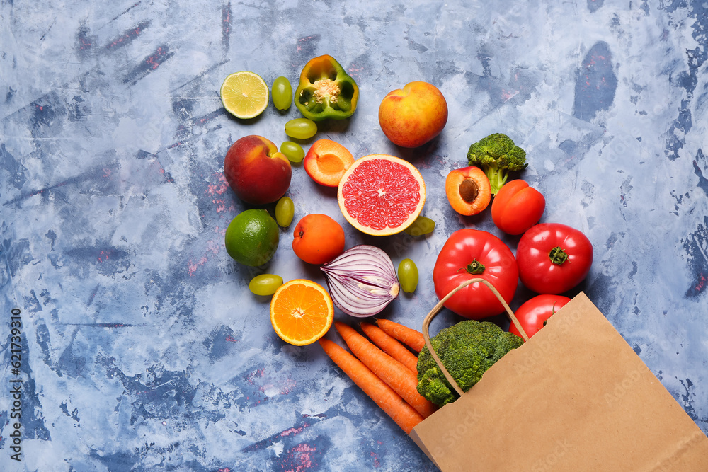 Paper bag with different fresh fruits and vegetables on blue background