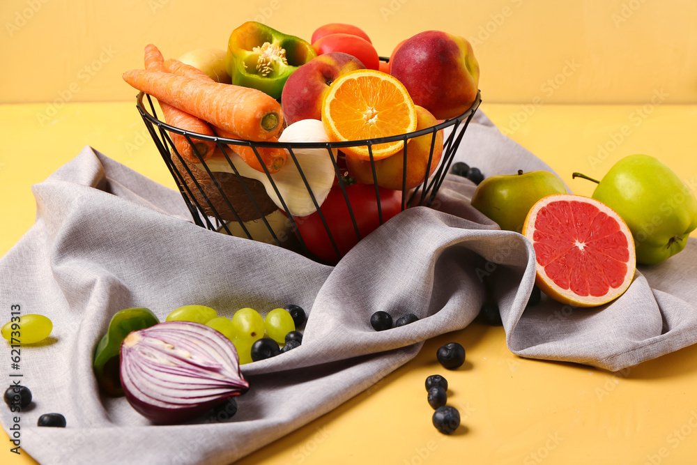 Basket with different fresh fruits and vegetables on yellow background