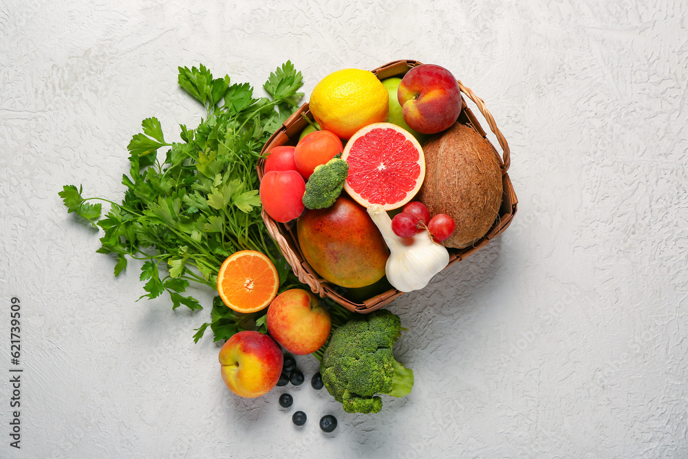 Wicker basket with different fresh fruits and vegetables on white background