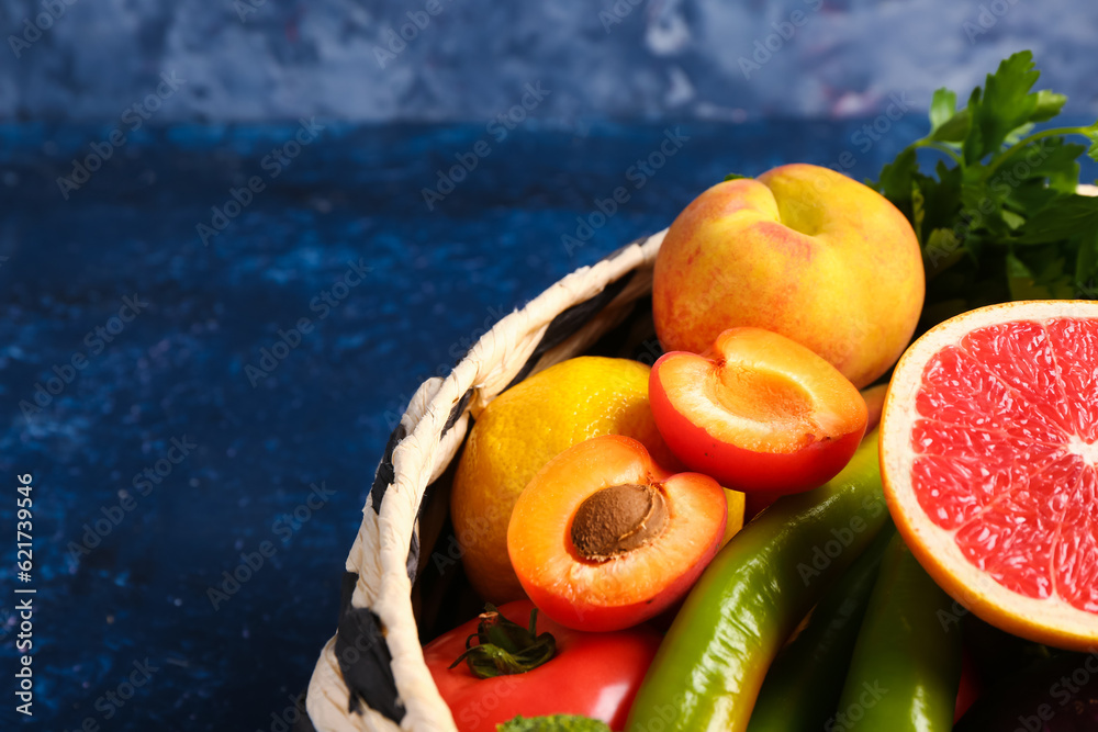 Wicker bowl with different fresh fruits and vegetables on blue background, closeup