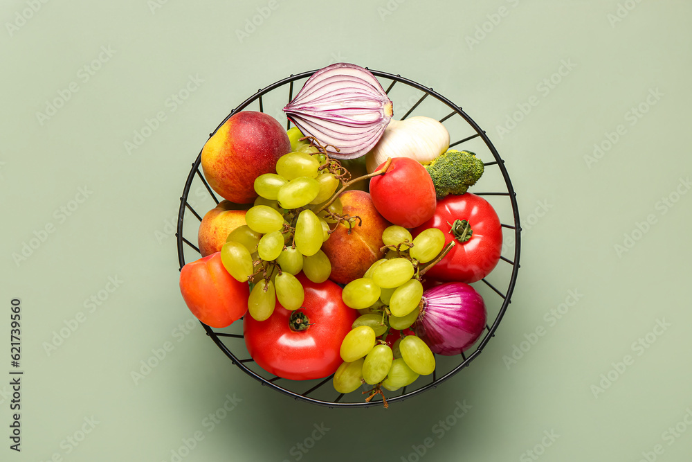 Basket with different fresh fruits and vegetables on green background