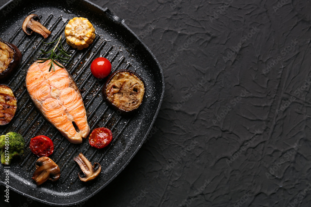 Frying pan with tasty grilled salmon steak and vegetables on black background