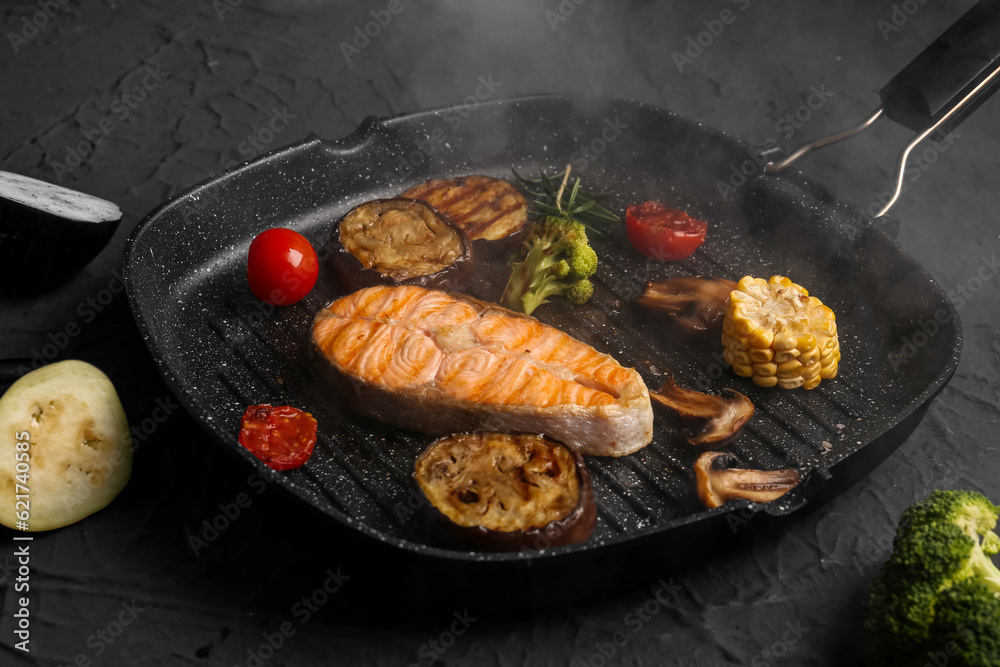 Frying pan with tasty grilled salmon steak and vegetables on black background