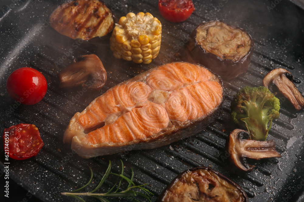 Tasty grilled salmon steak and vegetables in frying pan, closeup