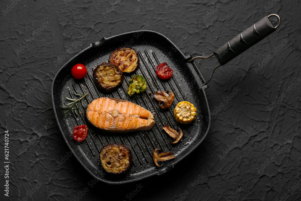 Frying pan with tasty grilled salmon steak and vegetables on black background