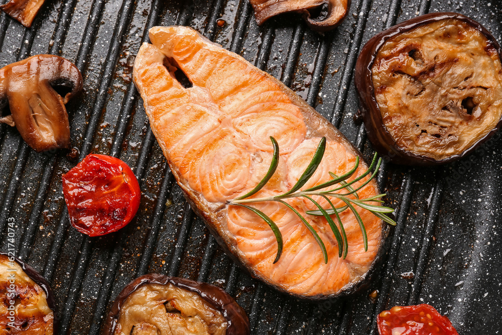 Tasty grilled salmon steak and vegetables in frying pan, closeup