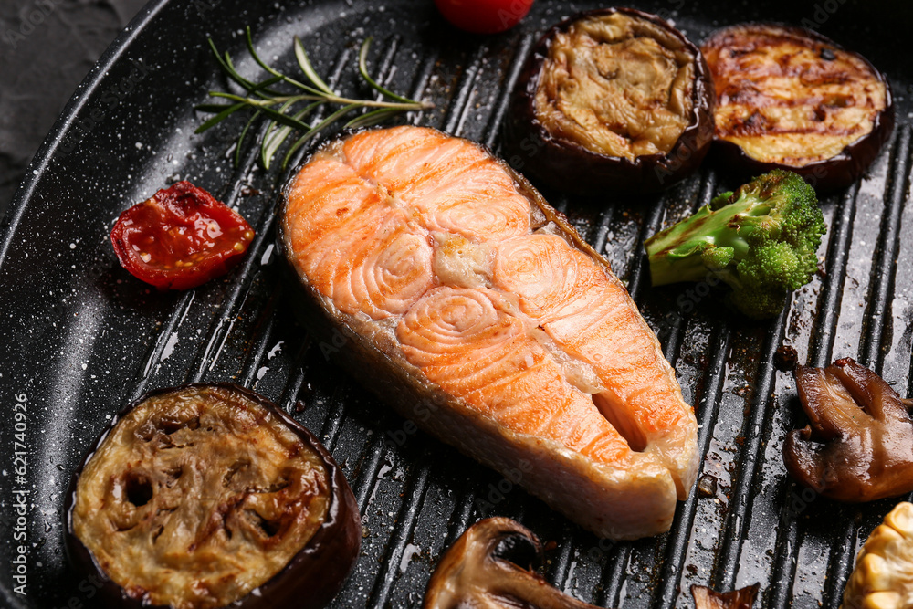 Frying pan with tasty grilled salmon steak and vegetables on table