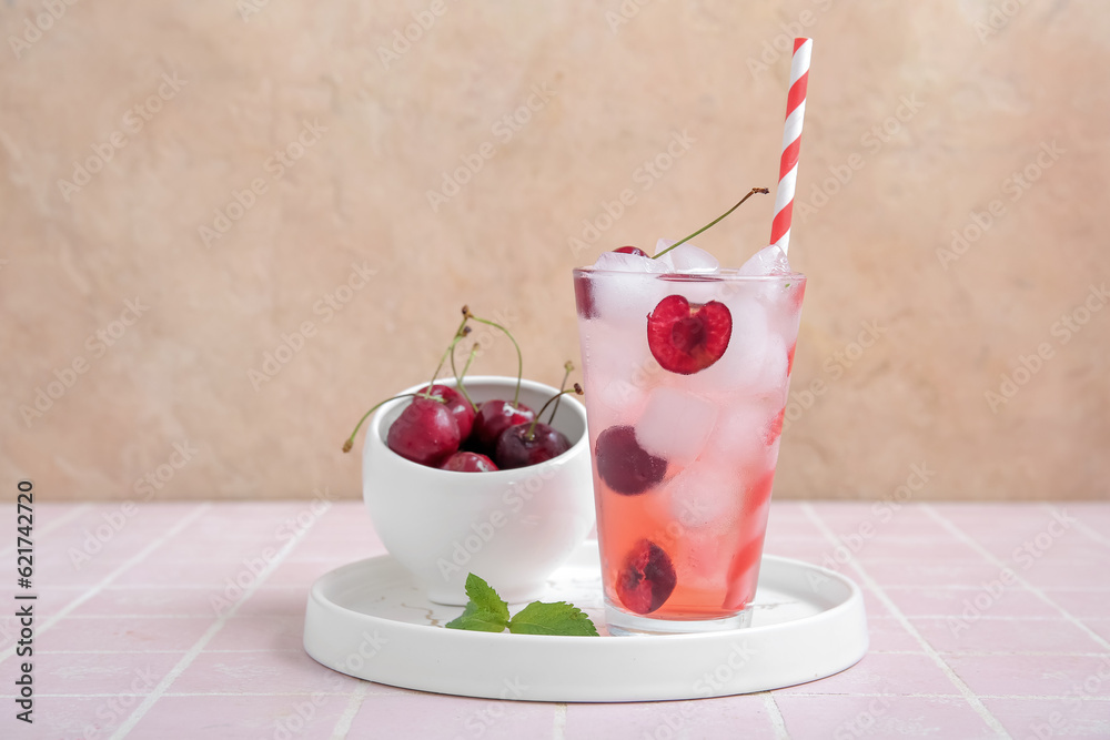 Glass of tasty cherry lemonade and bowl with berries on pink tile table