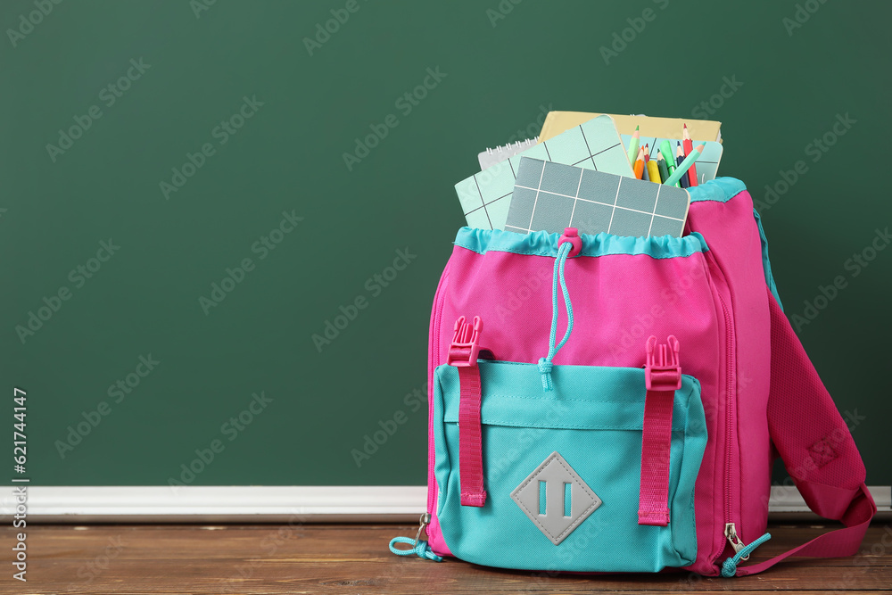 Colorful school backpack with notebooks and pencils on wooden table near green chalkboard