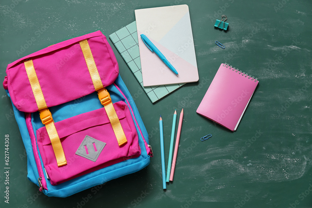 Colorful school backpack with notebooks, pen and pencils on green background