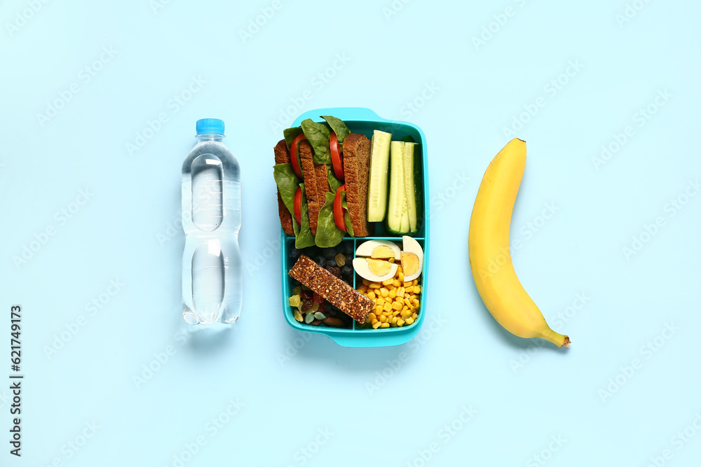 Bottle of water, banana and lunchbox with tasty food on blue background