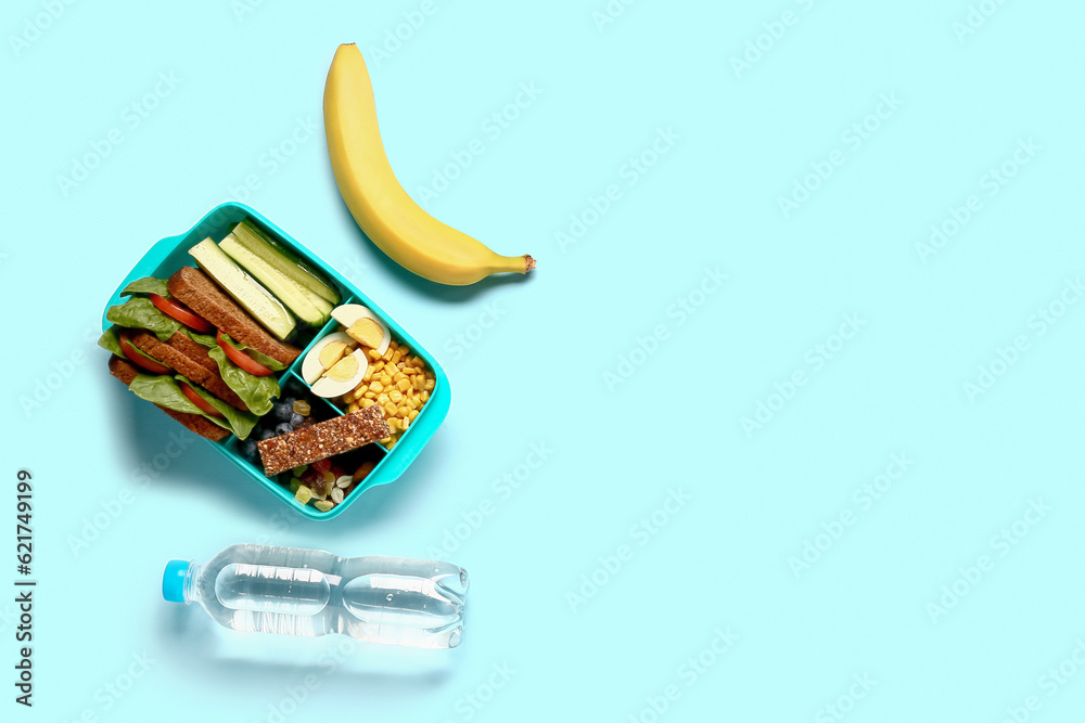 Bottle of water, banana and lunchbox with tasty food on blue background