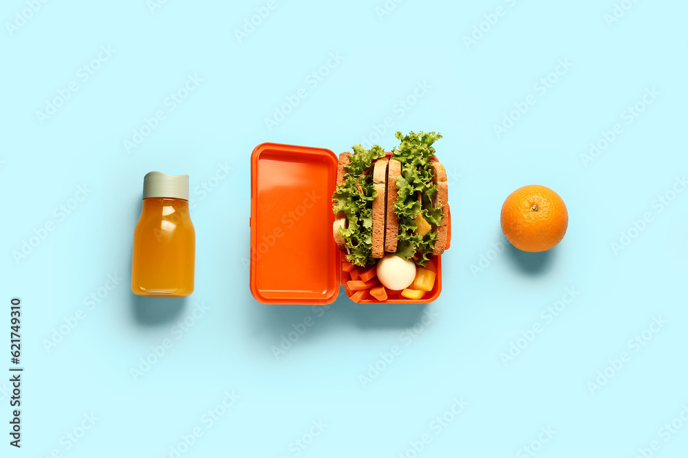 Bottle of juice, orange and lunchbox with tasty food on blue background