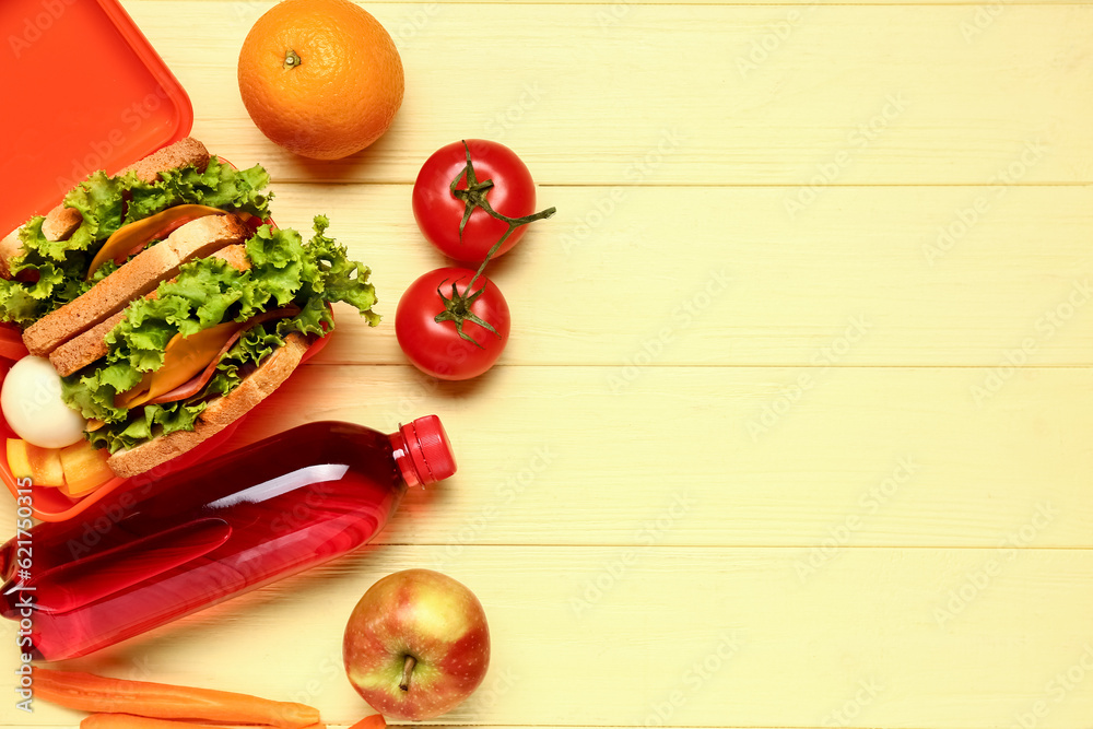 Bottle of juice and lunchbox with tasty food on yellow wooden background