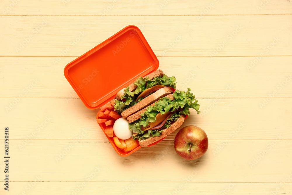 Apple and lunchbox with tasty food on yellow wooden background