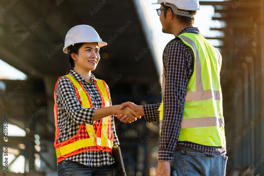 Asian female architect in protective helmets and wear reflective safety clothing are shaking hands w