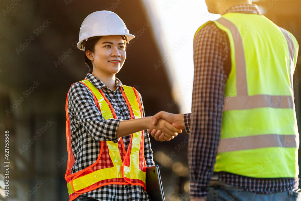 Asian female engineer in protective helmets and wear reflective safety clothing are shaking hands wi