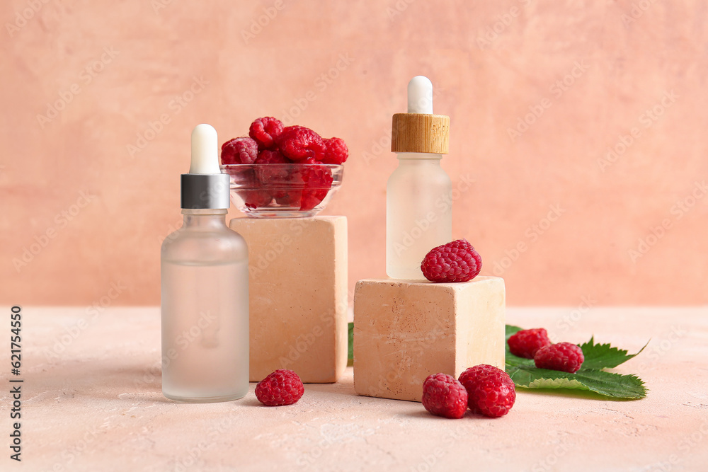 Decorative podiums with bottles of cosmetic raspberry oil on pink table