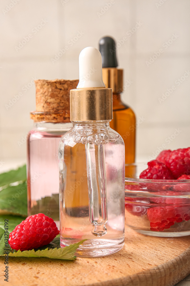 Wooden board with bottles of cosmetic raspberry oil, closeup