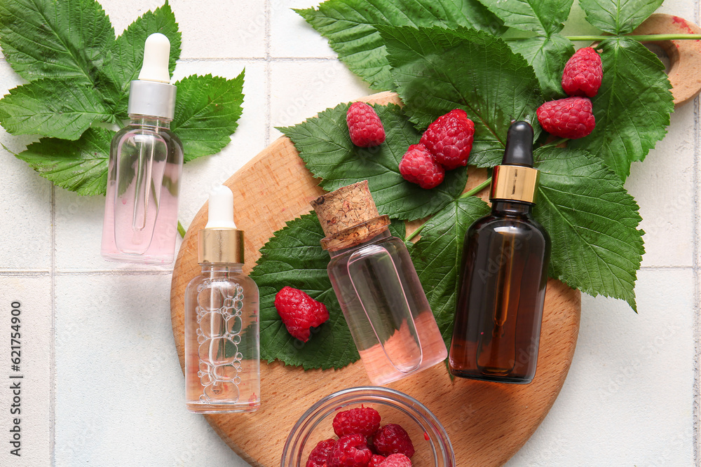 Wooden board with bottles of cosmetic raspberry oil on white tile background