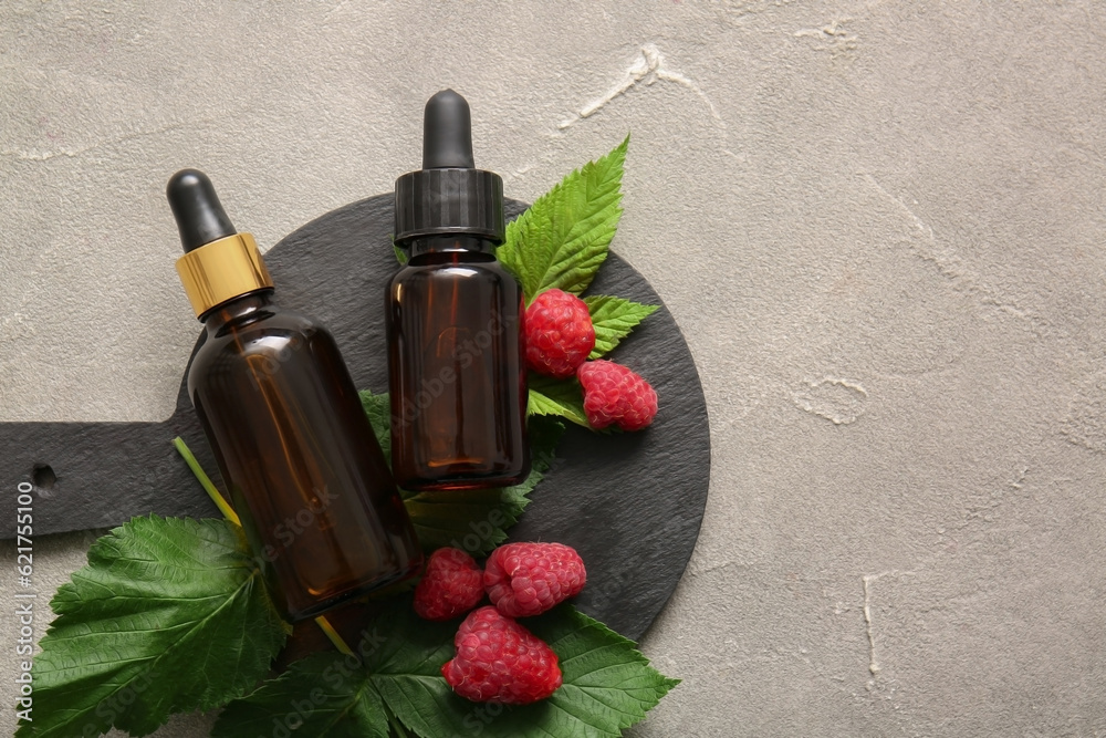 Board with bottles of cosmetic raspberry oil on grey table