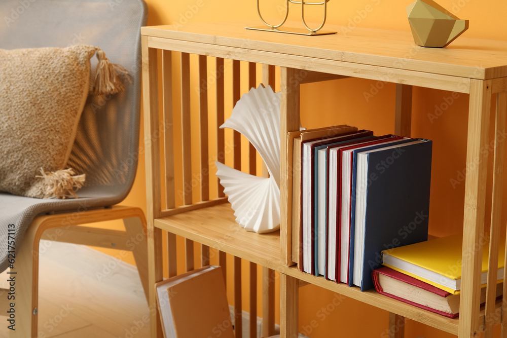 Shelving unit with books, decor and chair near orange wall in room, closeup