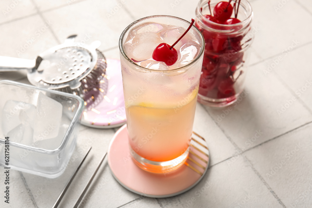 Glass of tasty cocktail with maraschino cherry on white tile background