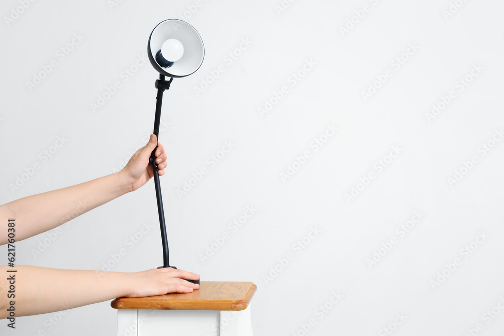 Woman with lamp on table against light background