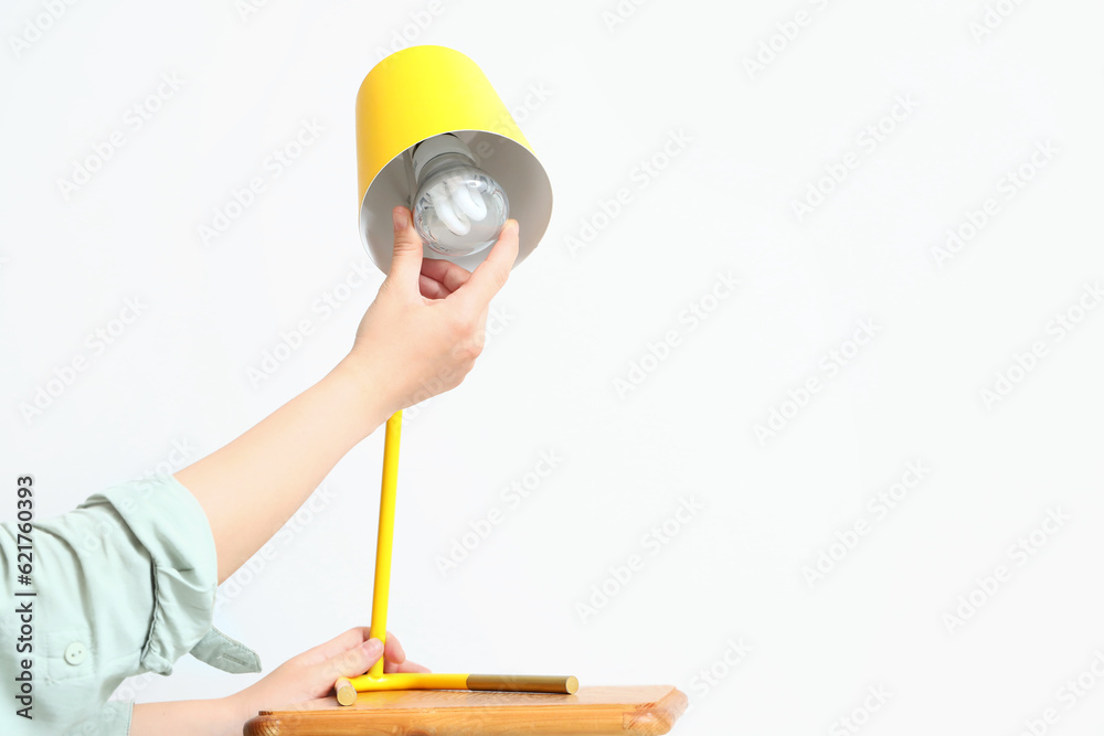 Woman changing light bulb in lamp on light background, closeup