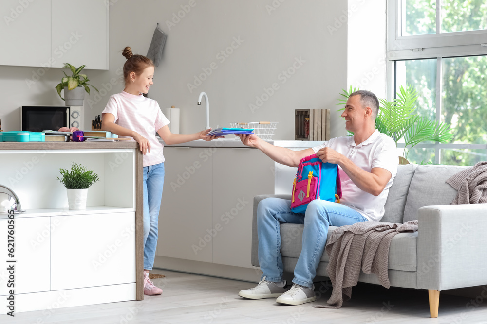 Father helping his little daughter to pack schoolbag in kitchen