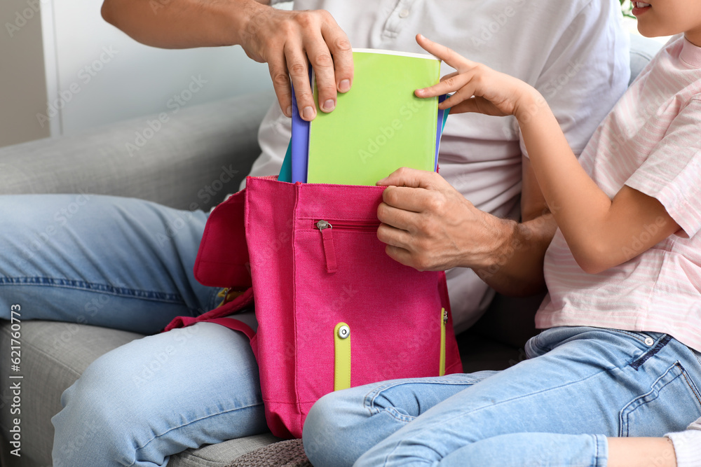 Father helping his little daughter to pack schoolbag at home, closeup