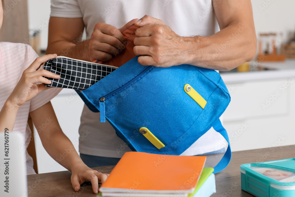 Father helping his little daughter to pack schoolbag in kitchen, closeup