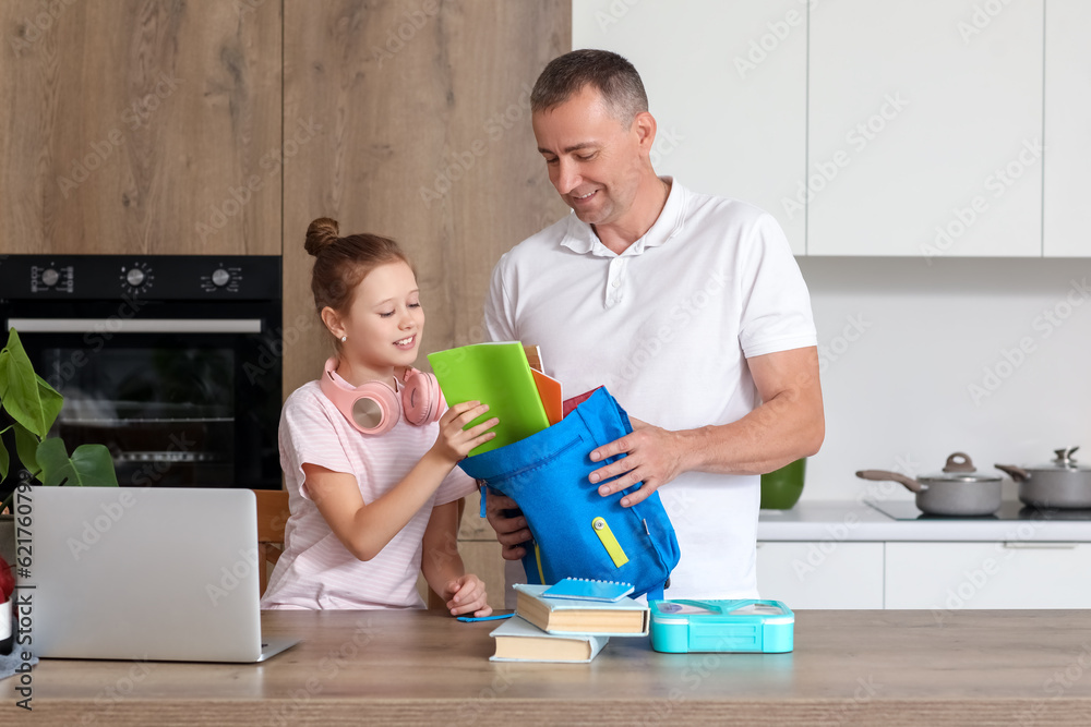 Father helping his little daughter to pack schoolbag in kitchen