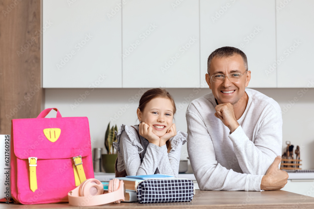 Father helping his little daughter to pack schoolbag in kitchen