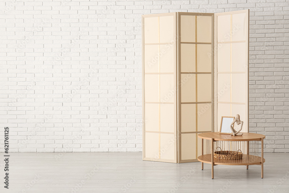 Folding screen and coffee table near white brick wall