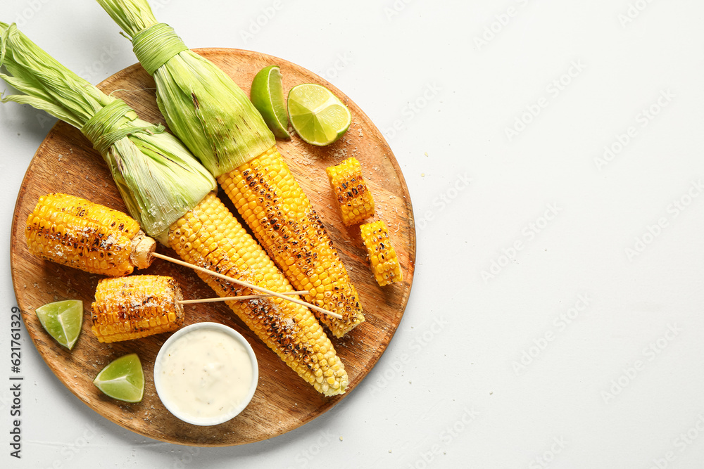 Wooden board with tasty grilled corn cobs and sauce on white background