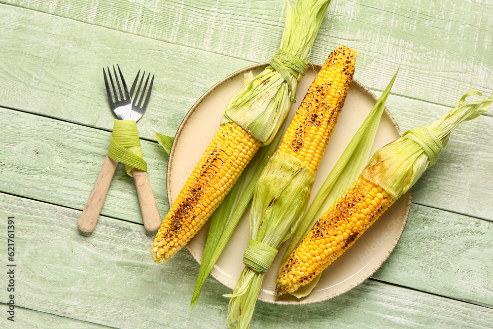 Plate with tasty grilled corn cobs on green wooden background