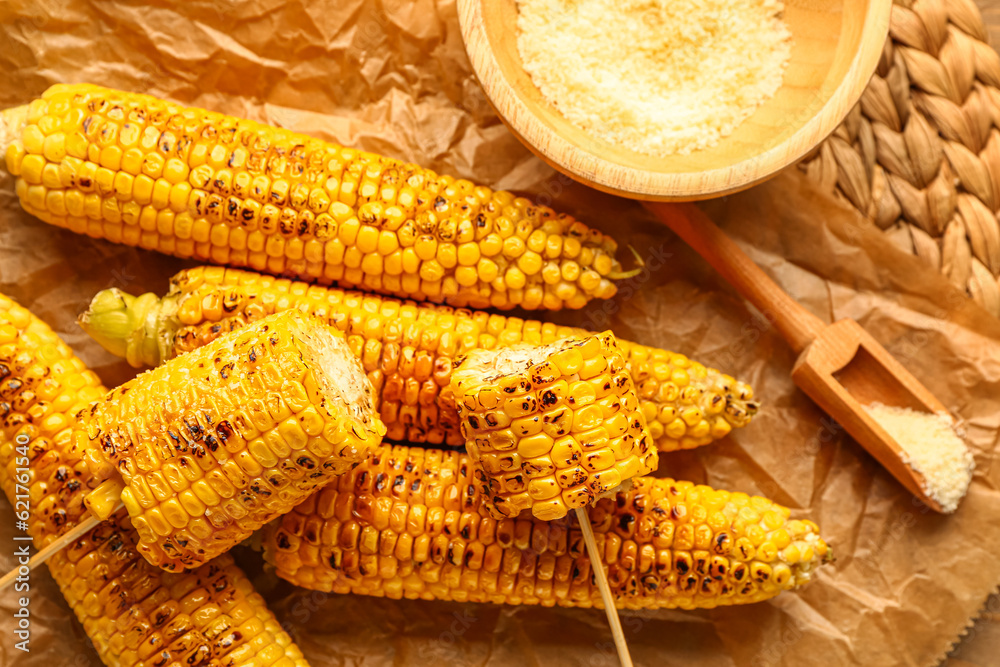 Baking paper with tasty grilled corn cobs and bowl of cheese, closeup