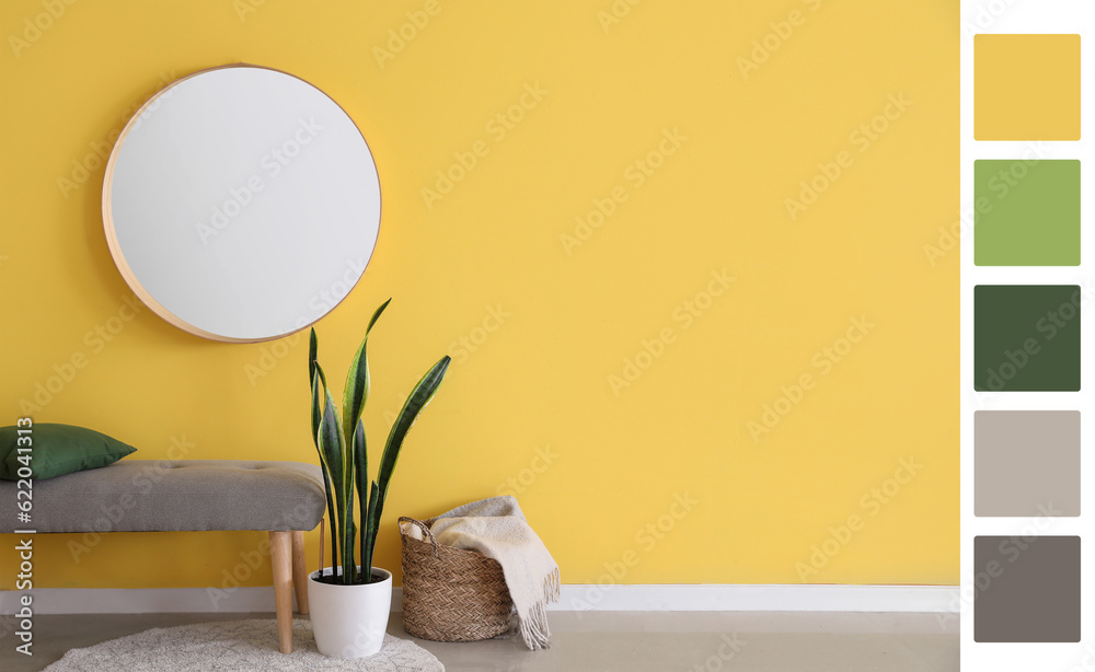 Interior of modern room with round mirror, soft bench, houseplant and basket near yellow wall. Diffe