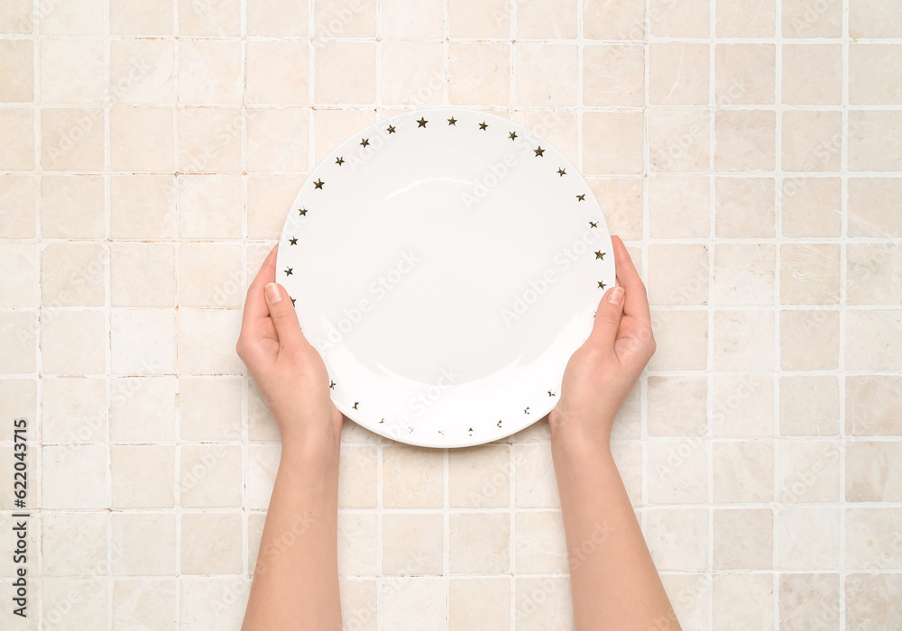 Female hands with empty plate on tile background