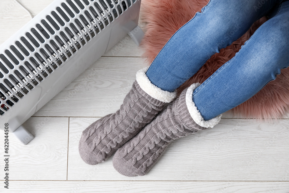 Woman in socks warming near radiator at home, closeup