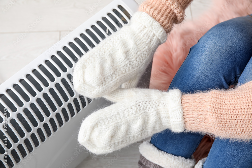 Woman warming hands in mittens near radiator at home, closeup