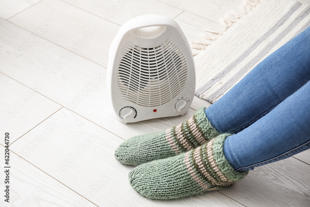 Woman warming legs in socks near electric fan heater at home, closeup