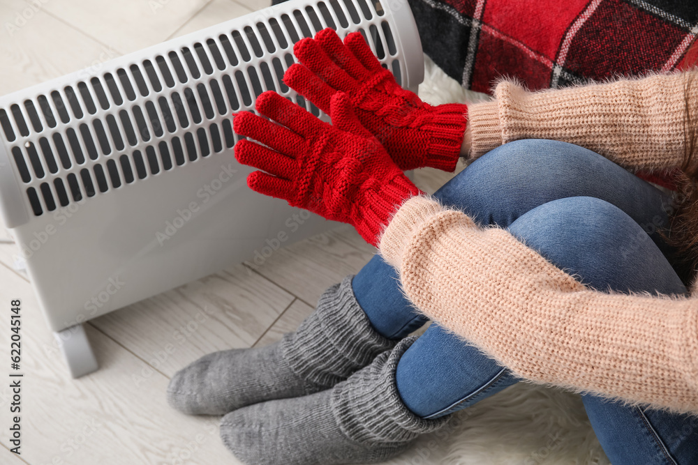 Woman warming hands in gloves near radiator at home, closeup